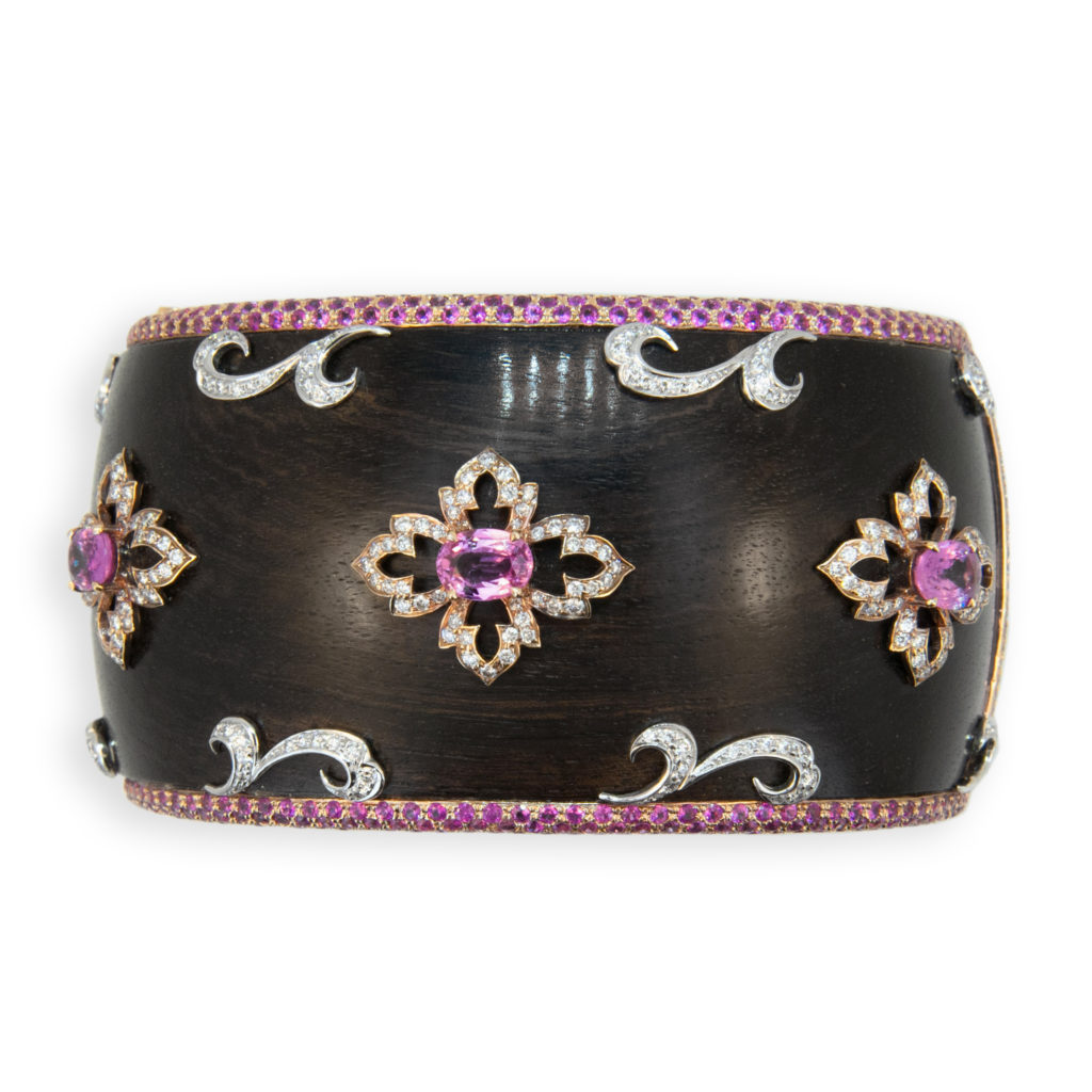 18 karat rose and white gold bangle bracelet, Grenadill wood bangle, 1.5 inches wide with pave' pink sapphire edge 604 pink sapphires 9.24 carats total weight. Bangle is set with three oval pink sapphires 3.08 carats total weight and 336 round diamonds are set in rose gold design surrounding three oval sapphires and in white gold design near pave' edge 1.97 carats total weight.