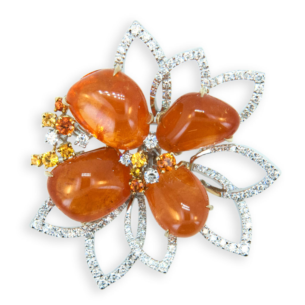 18 karat yellow and white gold brooch with four freeform tumble polished Mandarin Garnets 63.09 carats total weight. Ten Yellow and Orange Sapphires 0.82 carats total weight. 112 Round diamonds set with sapphires and in eight pointy leaf designs, 1.47 carats total weight.