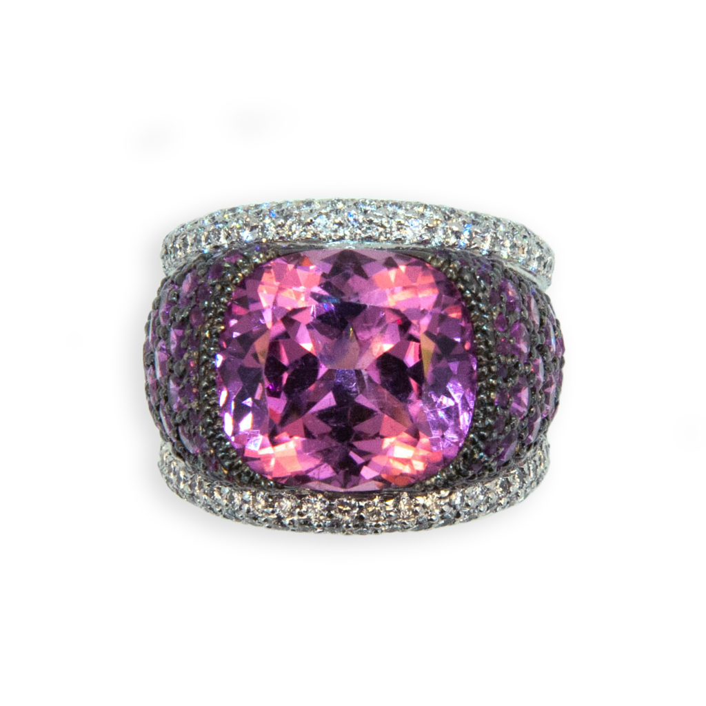 18 karat blackened white gold ring set with a cushion cut Pink tourmaline 12.65 carats total weight 14.68 x 13.72 x 9.36 mm, Surrounded by graduated cut and colored Pink Sapphires 5.86 carats total weight with two rows of diamonds 2.83 carats total weight on sides of shank. Ring is size 7 with a horseshoe.