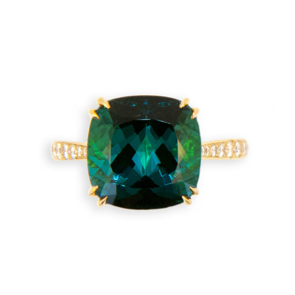 18 karat yellow gold ring, set in center is one faceted square cushion cut Indicolite Tourmaline 6.56cts. Shank and underbezel are set with 58 round diamonds .31 carat total weight. .8-1.6 mm. Tapered split prongs. Tourmaline measures 11.0 x 11.1 x 7.45 mm. Ring is a size 6 with a horseshoe.