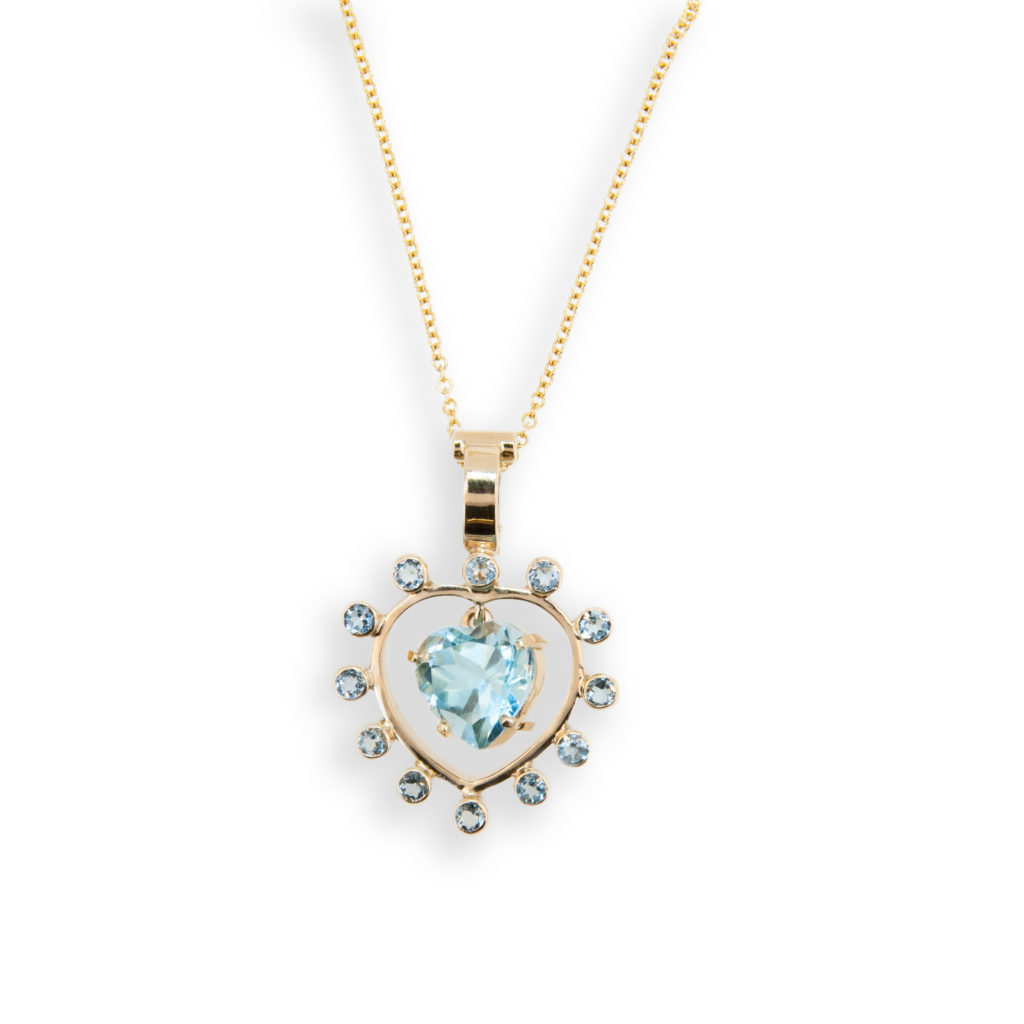 14 karat yellow gold Sweetheart pendant; heart shaped Blue Topaz 5.94 carats surrounded by twelve 2.8 mm round faceted blue topaz .99 carats total weight round blue topaz. Heart shaped blue topaz swings freely in center. Pendant bail opens and closes so can be used as an enhancer. Shown with a 14 karat yellow gold 18 inch 1.5 mm cable link chain with a lobster style clasp. Price shown is with chain but can be purchased without chain.